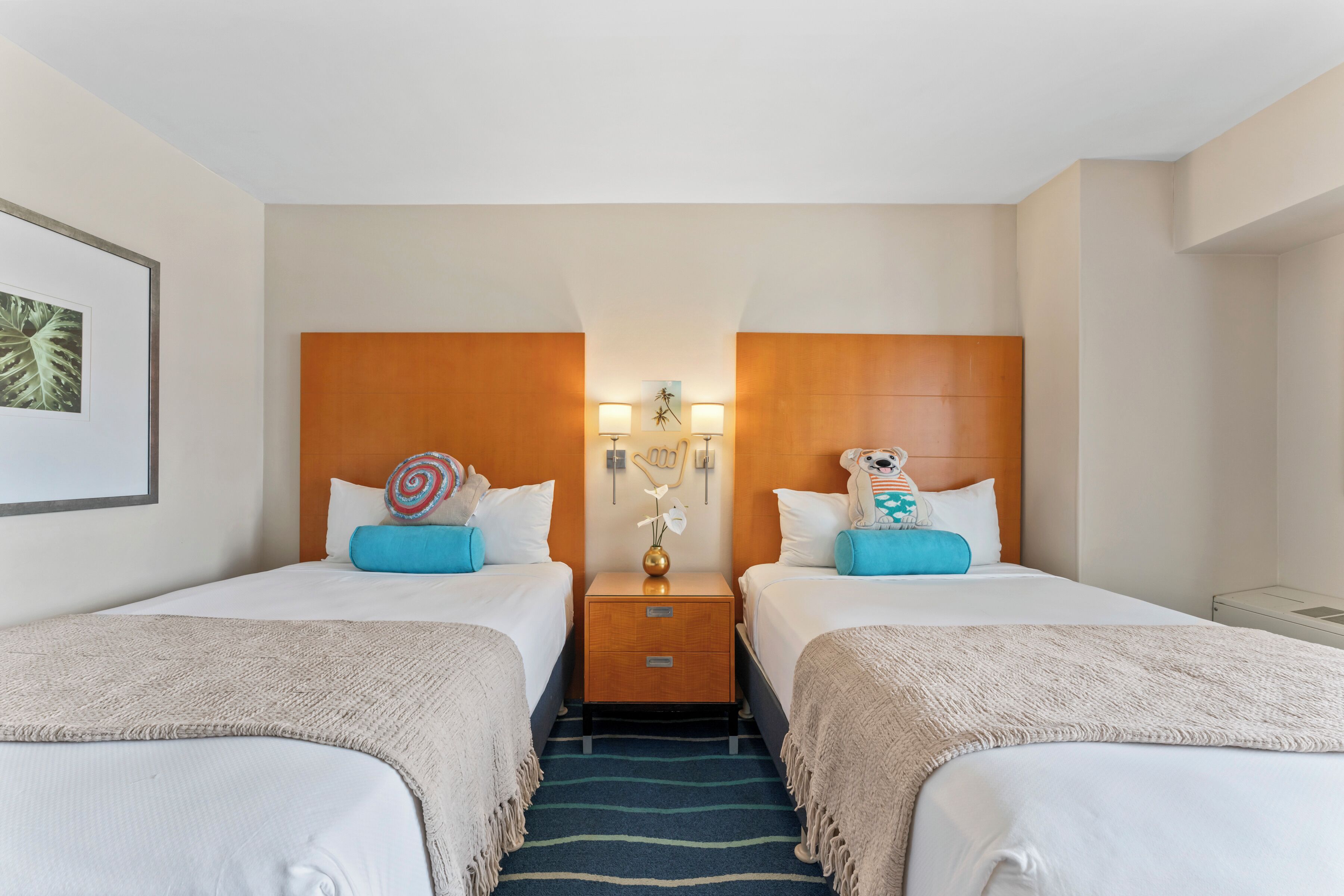 A hotel room with two beds, a nightstand with lamps, and a decorative wall piece.