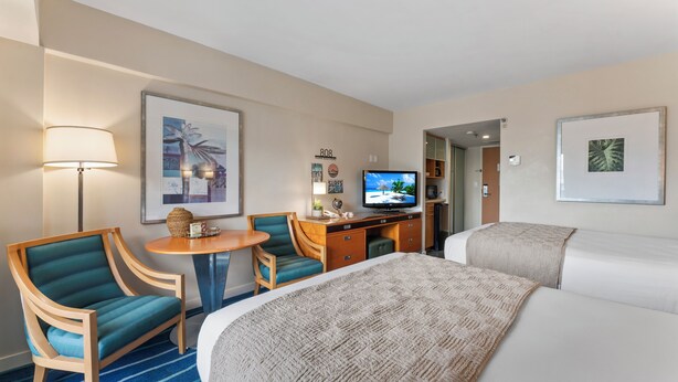 Una habitación de hotel con una cama, dos sillones, un escritorio con televisor y una lámpara.
