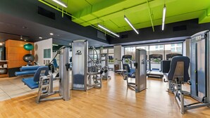 Un gimnasio con varios equipos de ejercicio, suelo de madera y luces de techo verdes.