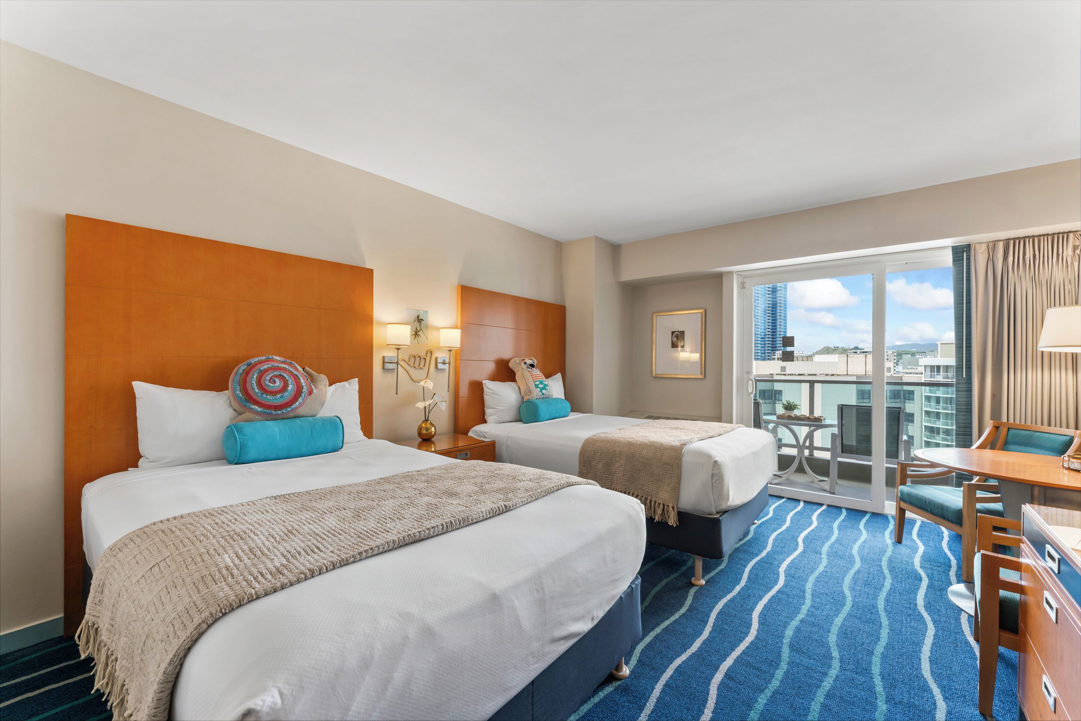 A hotel room with two beds, a balcony with a view, and a small dining area.