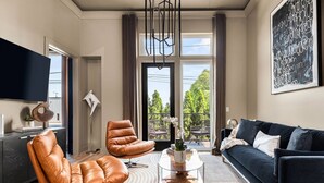 Una sala de estar moderna con sillones de cuero, un sofá oscuro, una mesa de centro de vidrio y un ventanal con vistas a árboles.