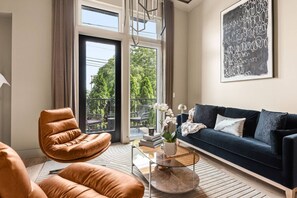 Un salon moderne avec un fauteuil en cuir, un canapé bleu foncé et une table basse en verre.