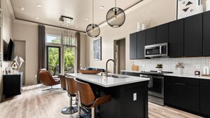 Una cocina moderna con una isla central, gabinetes negros, un microondas de acero inoxidable y un ventanal con vistas a zonas verdes.