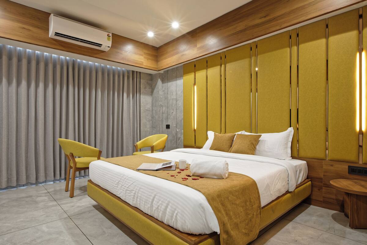 A modern bedroom with a large bed, two yellow chairs, a bedside table, and a wall-mounted air conditioner.