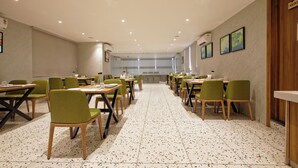A conference room with multiple tables and chairs, a tiled floor, and a view through the windows. - HOTEL PLENTEOUS INN  (Ahmedabad)