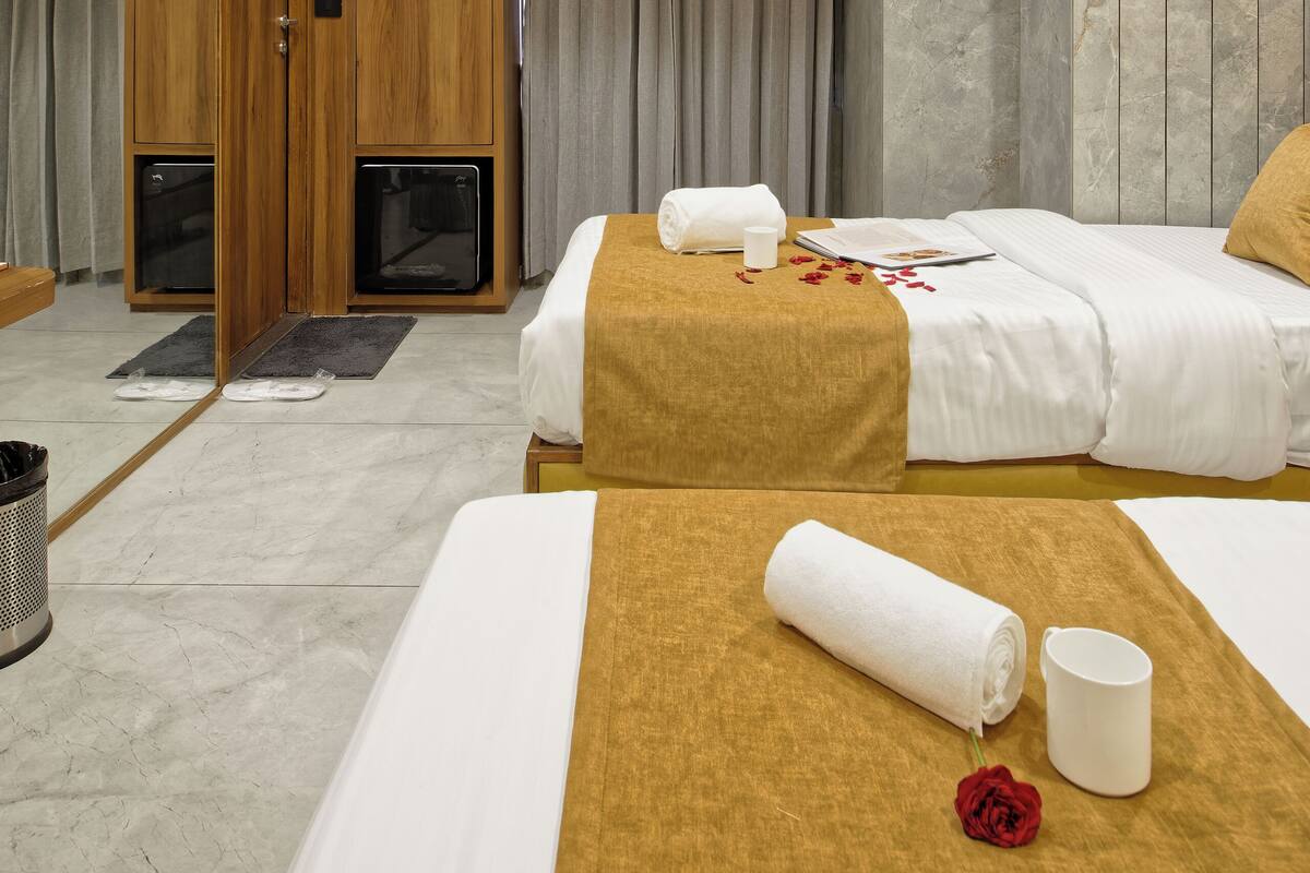 A hotel room with two beds, a wooden wardrobe, a mirror, and a ceiling-mounted air conditioner.