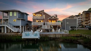 A waterfront property with a two-story building, a dock, and a small boat. - 4BR Waterfront Home w/ Private Dock and Ocean View (North Myrtle Beach)
