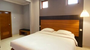 A bedroom with a large bed, two windows, a wooden headboard, a bedside table, and a door. - Pilatus Hotel Bandung (Bandung)