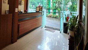 A hotel reception area with a wooden reception desk, a glass door leading outside, and a tiled floor. - Pilatus Hotel Bandung (Bandung)