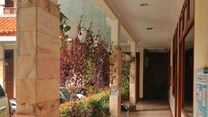 A corridor with tiled flooring, a tiled wall, and a hanging plant arrangement. - Pilatus Hotel Bandung (Bandung)
