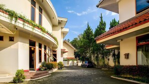 A courtyard with a paved walkway, buildings with balconies, and a parked car. - Pilatus Hotel Bandung (Bandung)