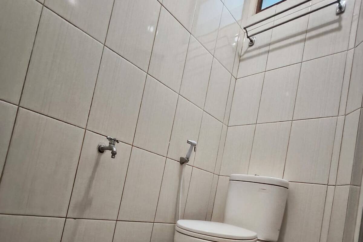 A small, tiled bathroom with a toilet and two faucets.