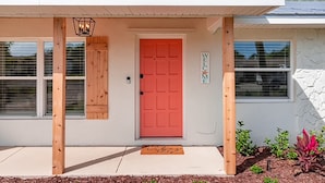 A house with a red door, a welcome sign, and a wooden porch.