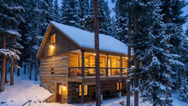 A log cabin with a balcony, surrounded by snow-covered trees.