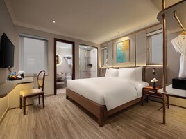 Hotelkamer met een groot bed, een bureau met stoel, een televisie en een zichtbare badkamer door een open deur.