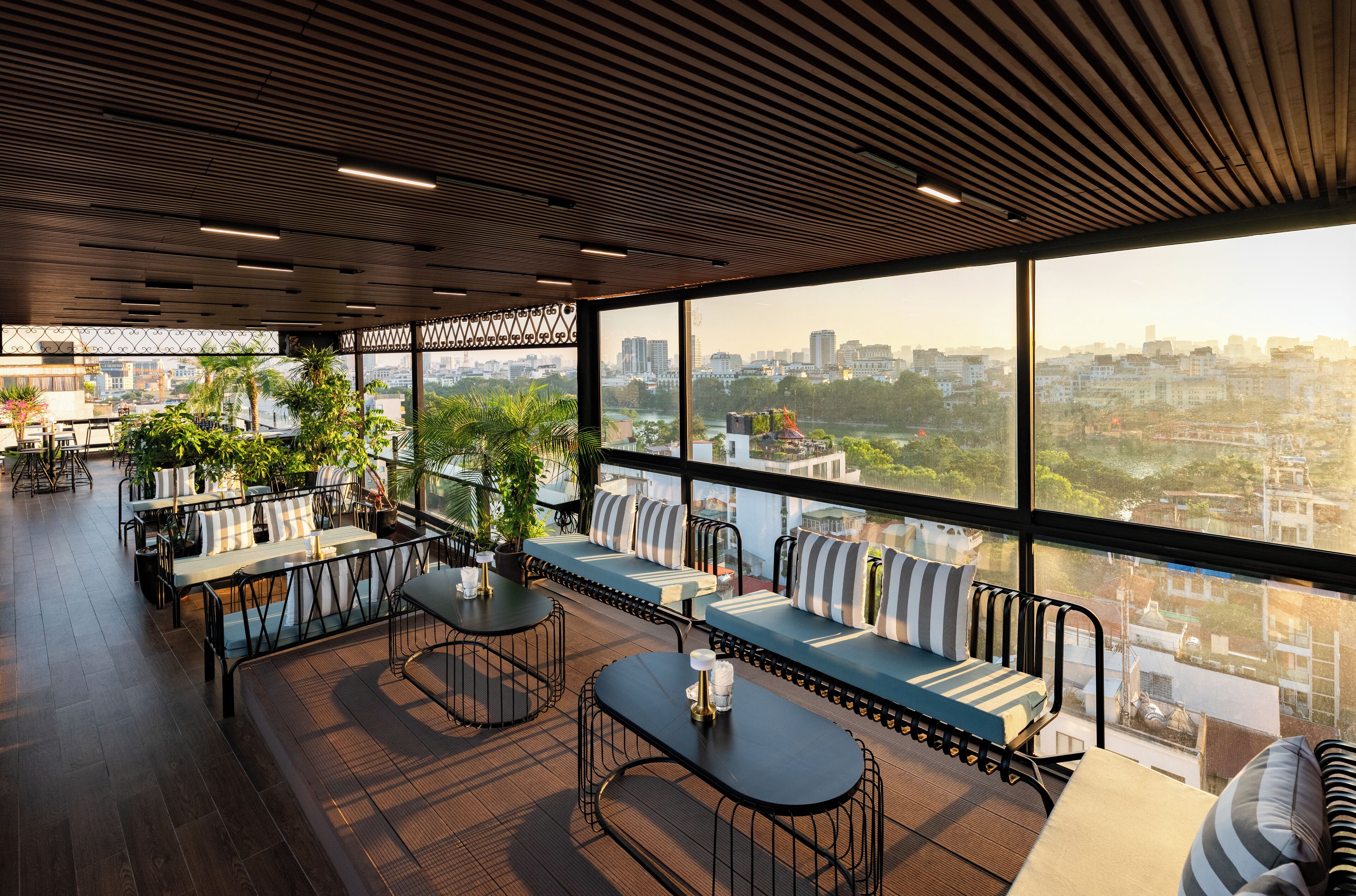 A modern rooftop lounge with seating areas, large windows offering city views, and a wooden ceiling.