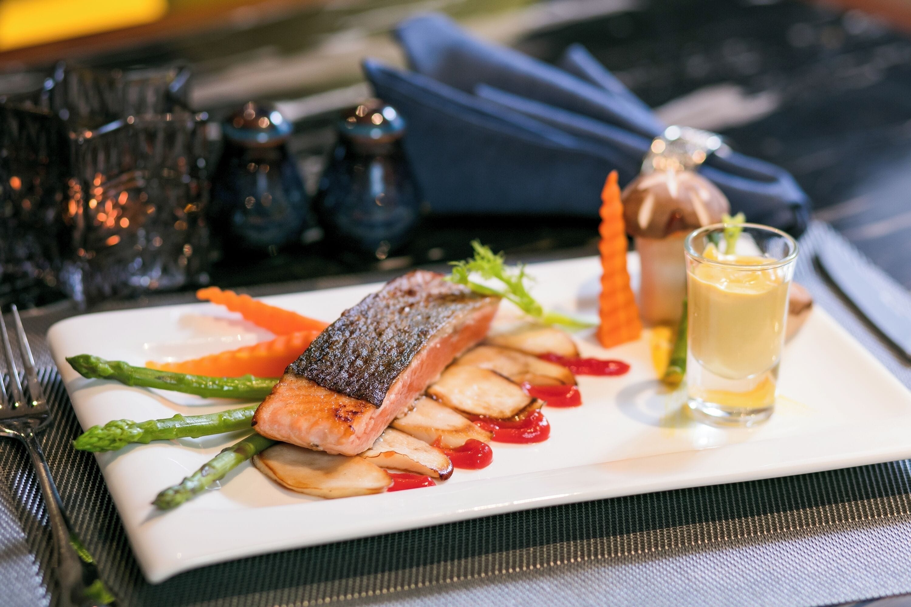 A plate of food with salmon, asparagus, and carrots, accompanied by a glass of sauce.
