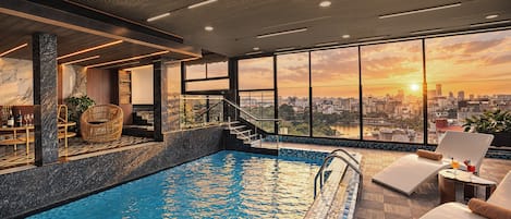 A rooftop infinity pool with a city view, a lounge area with chairs, and a staircase leading to an upper level.