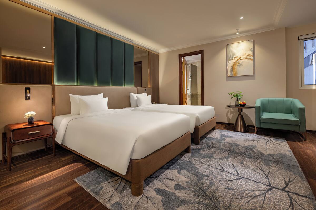 A hotel room with two beds, a small side table, a chair, a mirror, and a painting on the wall.