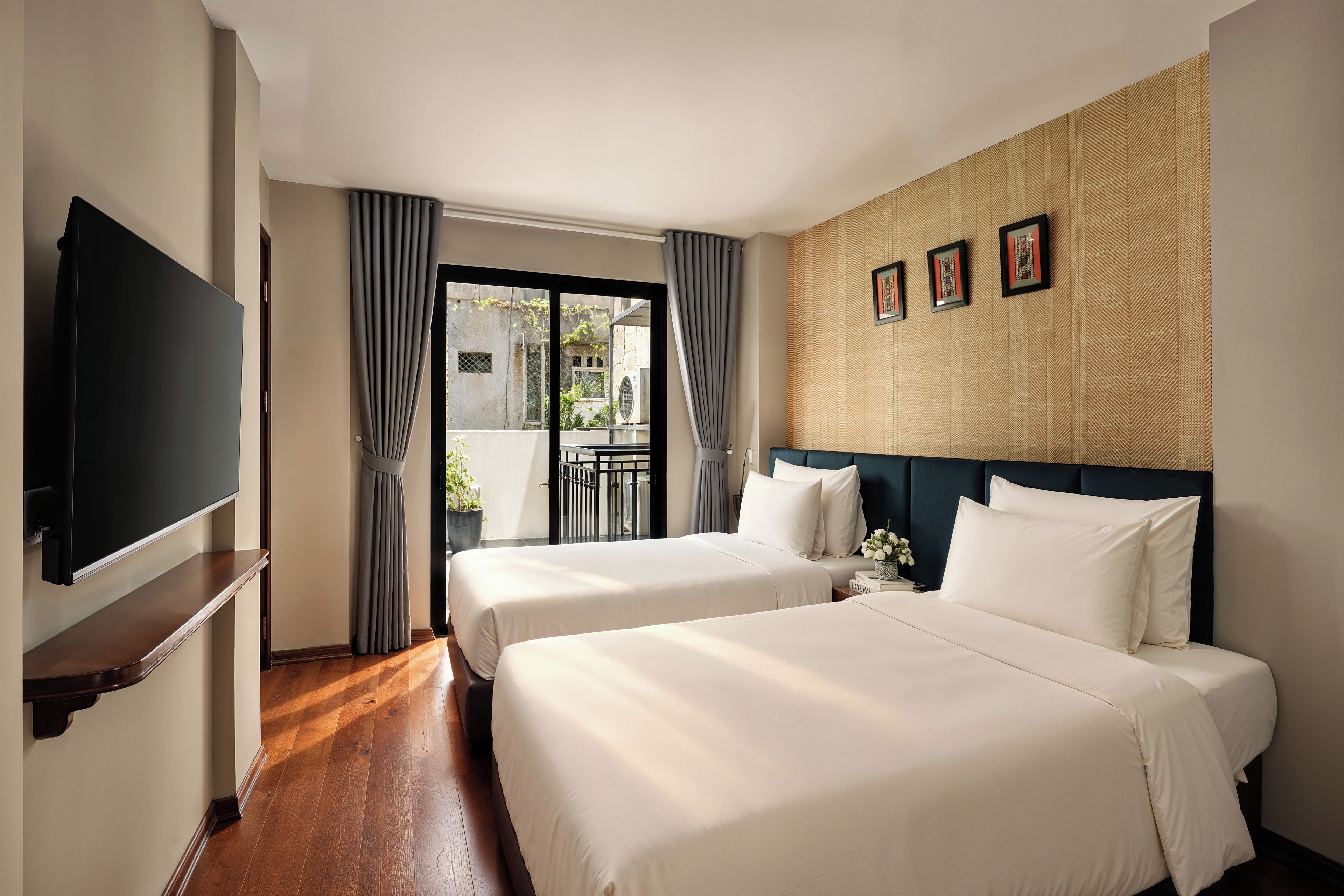 A hotel room with two beds, a television, a balcony with curtains, and a patterned wall.