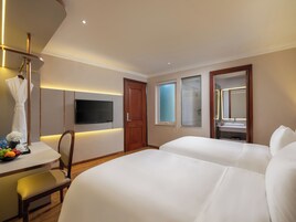 Habitación de hotel con cama, escritorio, silla, televisión, puerta y ventana.