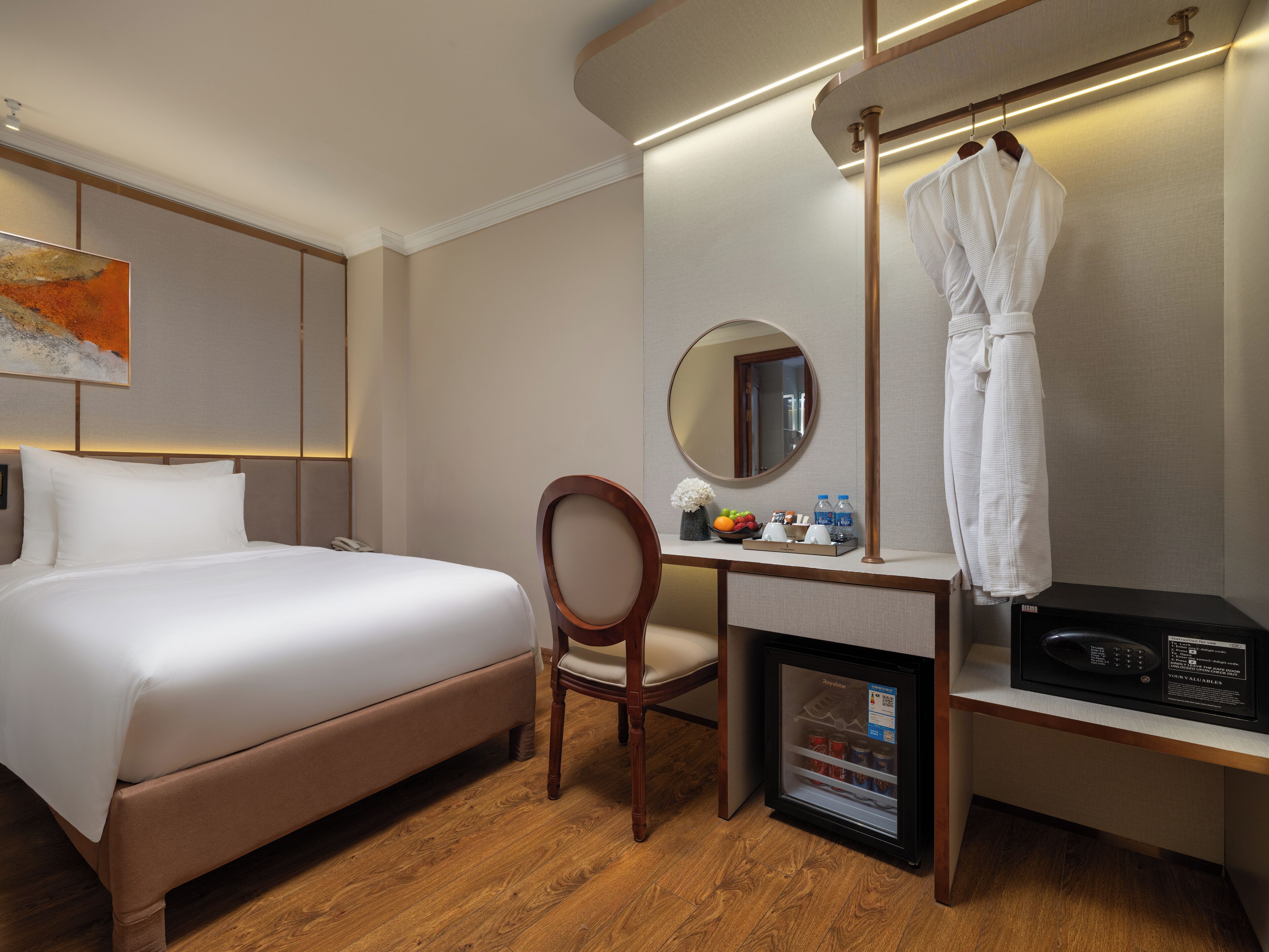 Habitación de hotel con cama, escritorio, silla, espejo, bata colgada en un perchero y un minibar.