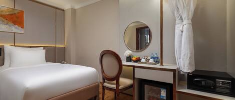 Habitación de hotel con cama, escritorio, silla, espejo, bata colgada en un perchero y un minibar.
