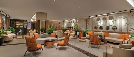 A spacious lobby with multiple seating areas, including sofas and chairs, and a variety of plants.