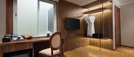 Ett hotellrum med ett skrivbord i trä, en stol, en minibar, en tv och en badrock som hänger på en träpanel.