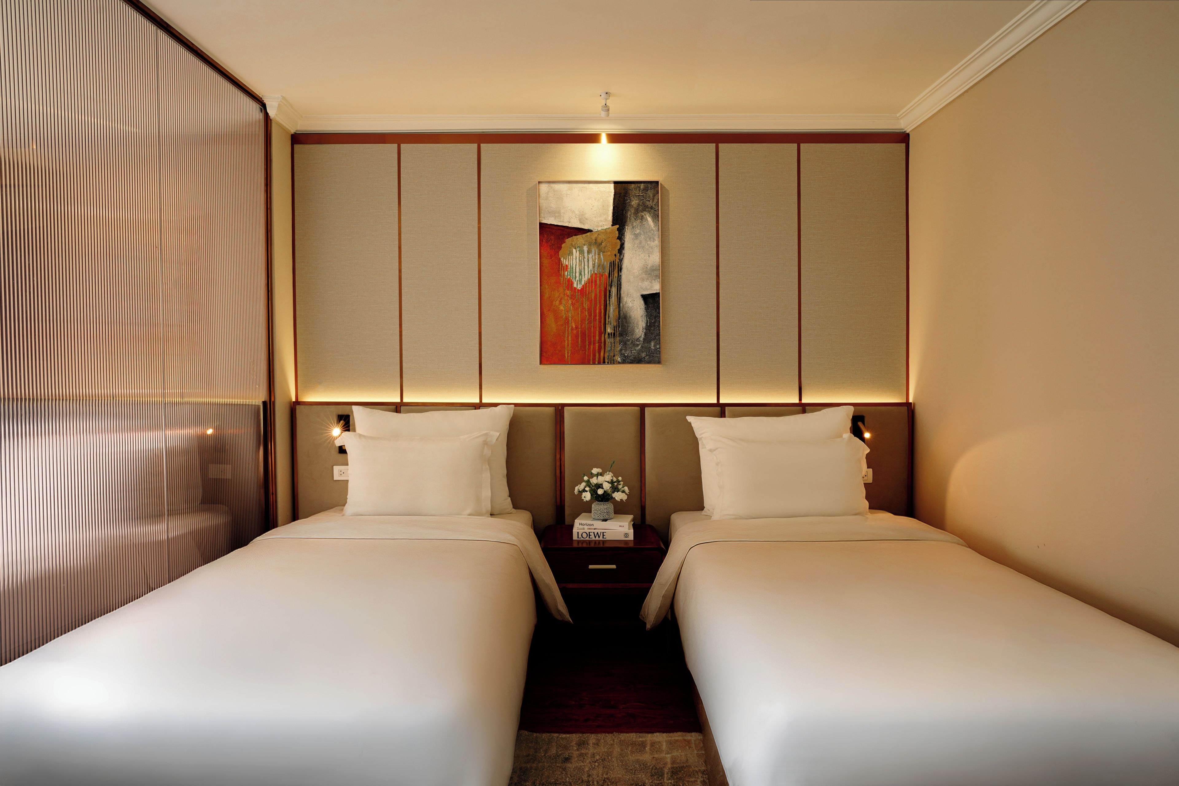 Habitación de hotel con dos camas, un cuadro en la pared y una mesita de noche con un florero.