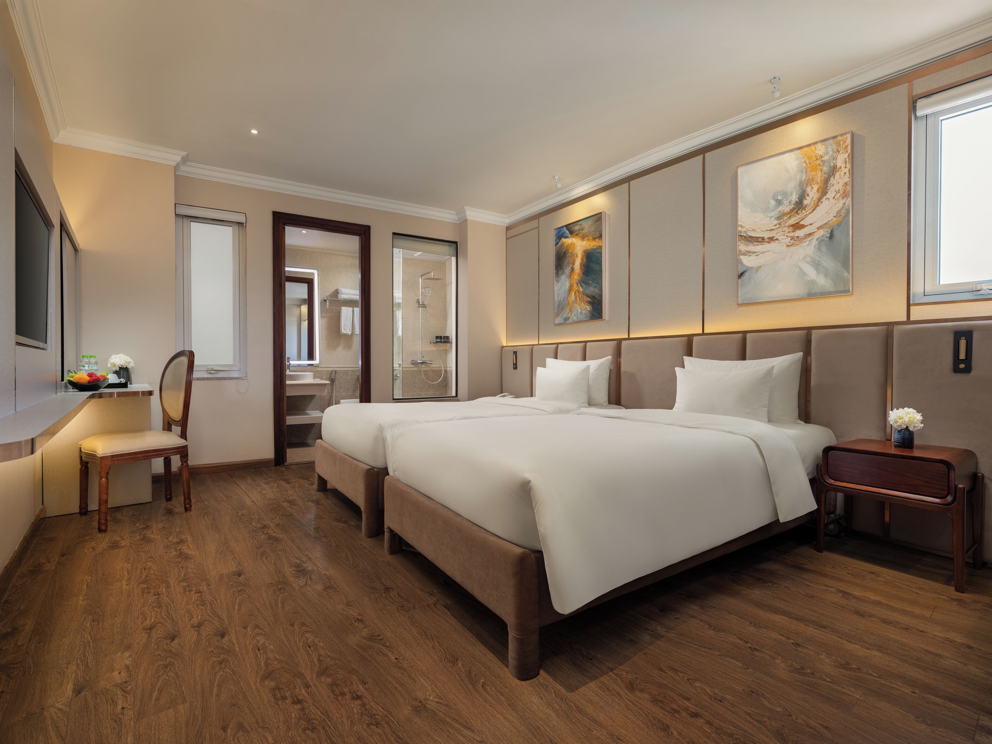 A spacious hotel room with a large bed, a bedside table, a chair, a desk with a bowl of fruit, and a bathroom visible through an open door.