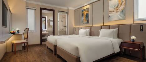 Amplia habitación de hotel con una cama grande, una mesita de noche, una silla, un escritorio con un frutero, y un baño visible a través de una puerta abierta.
