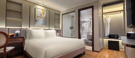 Una habitación de hotel moderna con una cama grande, un escritorio con una silla, una mesita de noche con un florero, un baño con ducha, inodoro y televisor.
