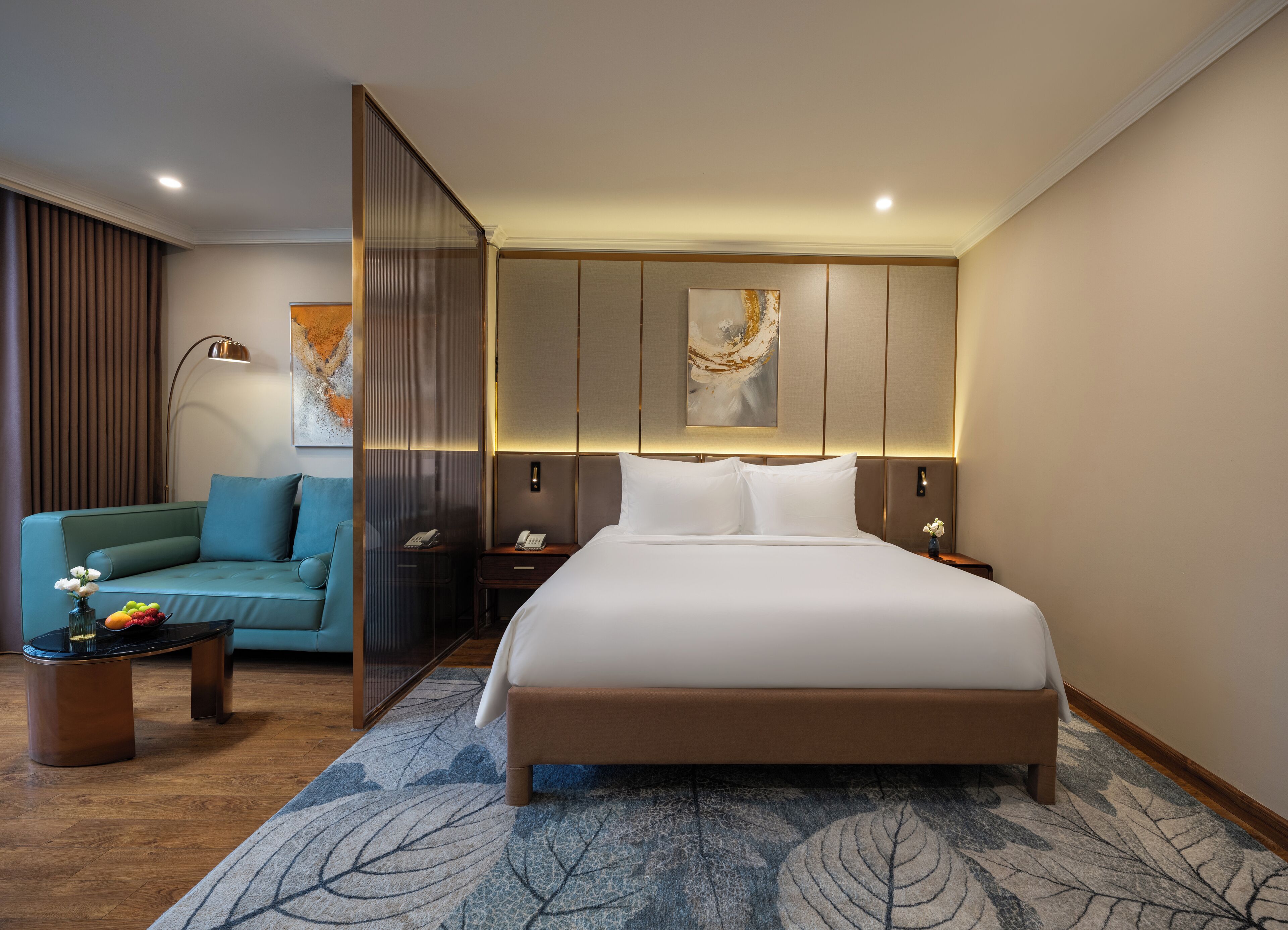 A modern hotel room with a large bed, a sofa, a coffee table, and a decorative wall piece.