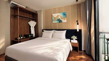 A hotel room with a large bed, a wooden wardrobe, a painting on the wall, and a nightstand with a lamp.