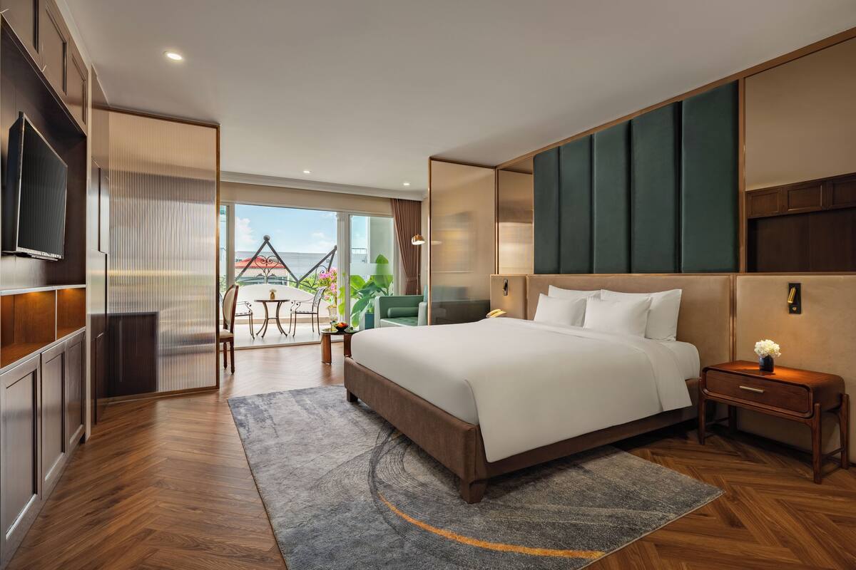 A modern hotel room with a large bed, a TV, a desk, and a balcony with a view.
