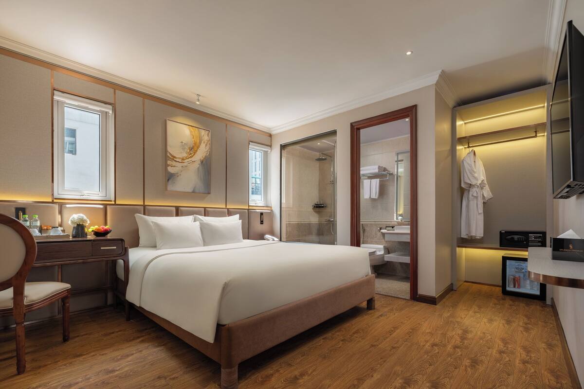 A hotel room with a large bed, a desk, a chair, a vanity with a mirror, and a robe hanging on the wall.