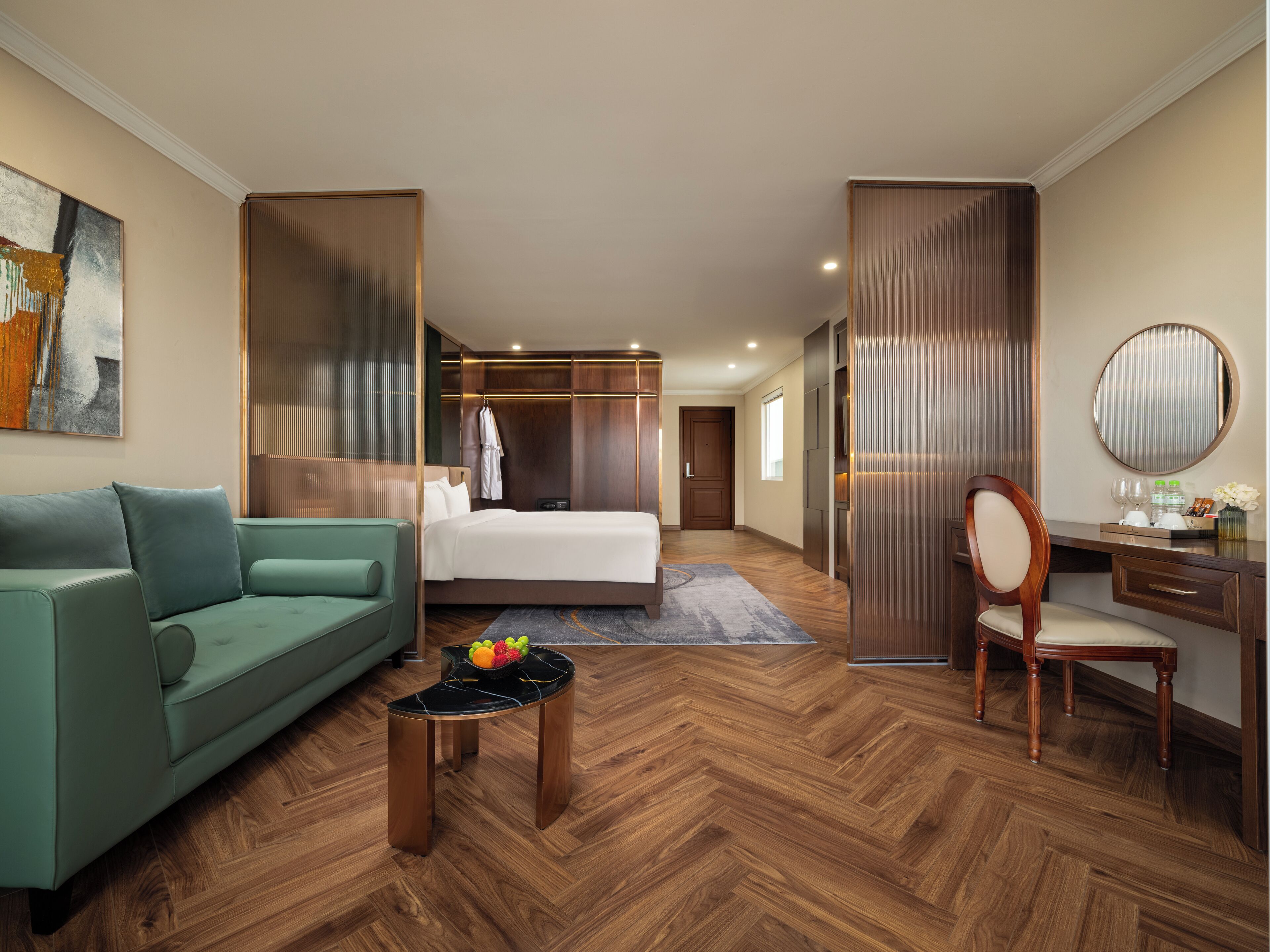 Una habitación de hotel con una cama, un sofá verde, un escritorio con una silla, un espejo redondo y un frutero sobre una mesita.