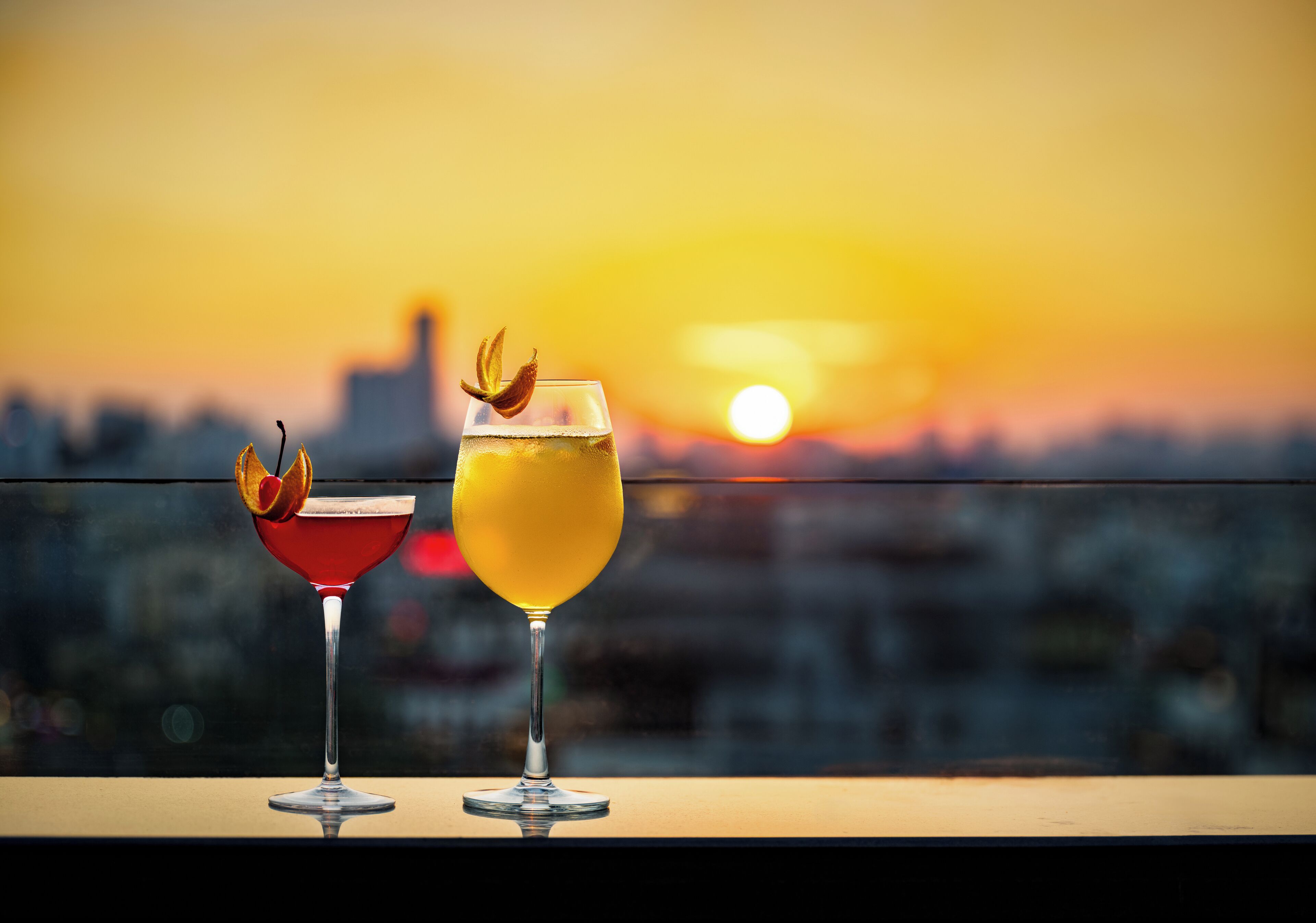 Two cocktails on a balcony with a sunset view.