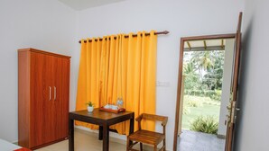 A room with a bed, a wooden wardrobe, a table with a tray of items, a chair, and a door leading to a garden. - The Regency villa by Escape Essence  (Unawatuna)