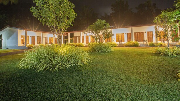 A well-lit building with a symmetrical facade, surrounded by manicured lawns and trees. - The Regency villa by Escape Essence  (Unawatuna)