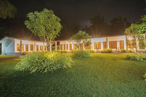 A well-lit building with a symmetrical facade, surrounded by manicured lawns and trees. - The Regency villa by Escape Essence  (Unawatuna)