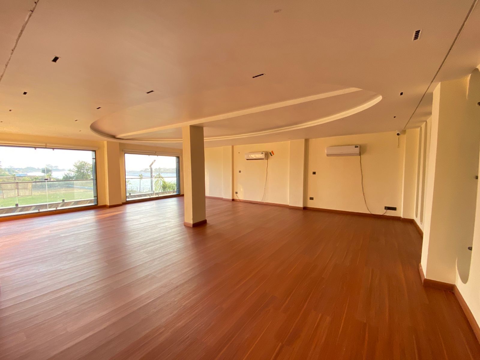 Una habitación amplia con piso de madera, ventanas grandes que ofrecen vistas al exterior y unidades de aire acondicionado integradas.