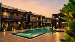 A swimming pool with a wooden deck, surrounded by a multi-story building with balconies and outdoor lighting. - Evaara By The Ganges - River Side Resort and Villa (Haridwar)