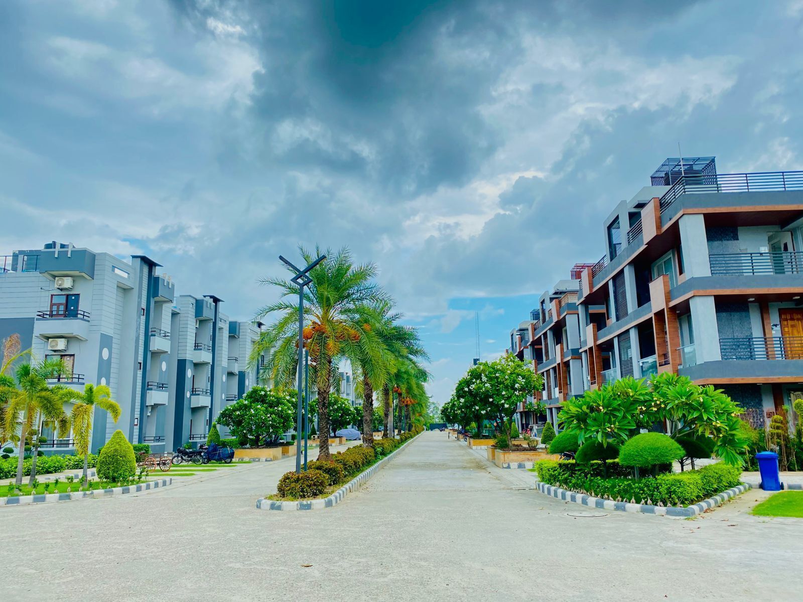 Una calle urbana moderna con edificios residenciales de varios pisos, palmeras y un cielo despejado.