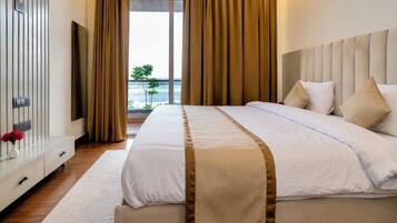 Una habitación de hotel con cama, mesita de noche con un jarrón de flores, ventana grande con cortinas y vistas al exterior.