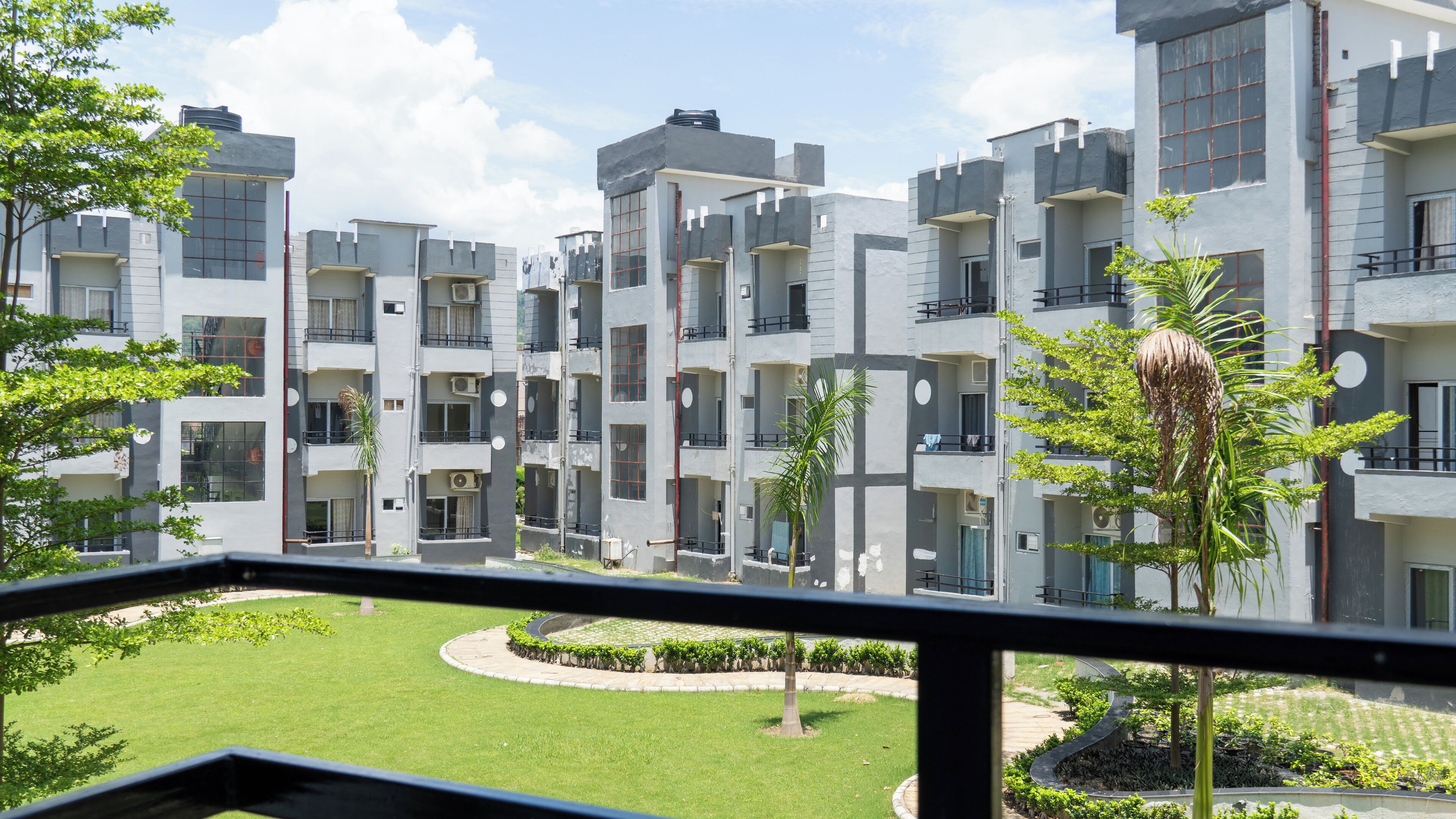 A modern multi-story residential building with balconies, a courtyard, and surrounding greenery.