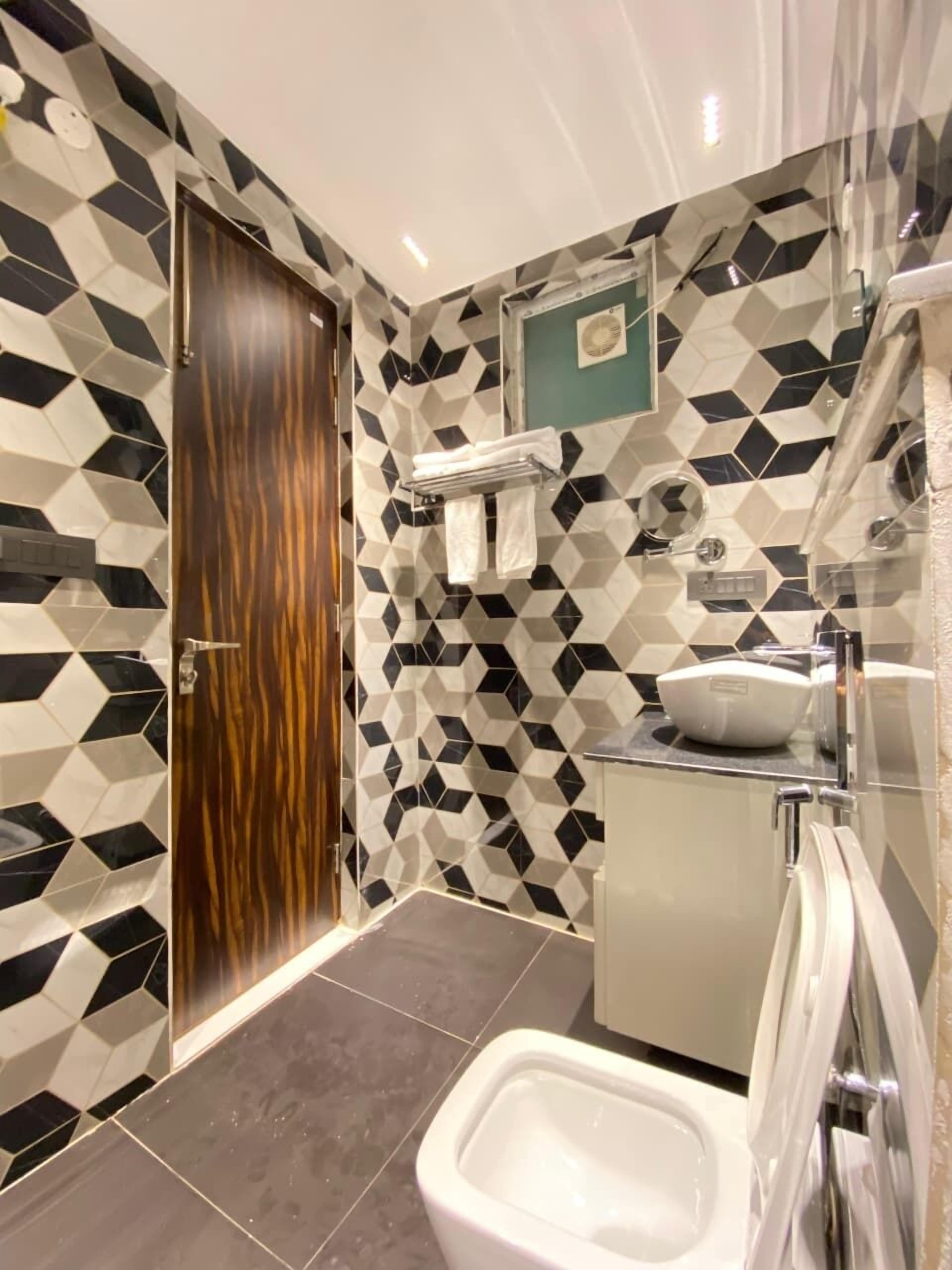 Un baño con un diseño geométrico de azulejos, una puerta de madera, un lavamanos blanco y un bidé.