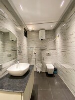 Un baño moderno con paredes de mármol, un lavamanos grande, un bidé y una ducha.
