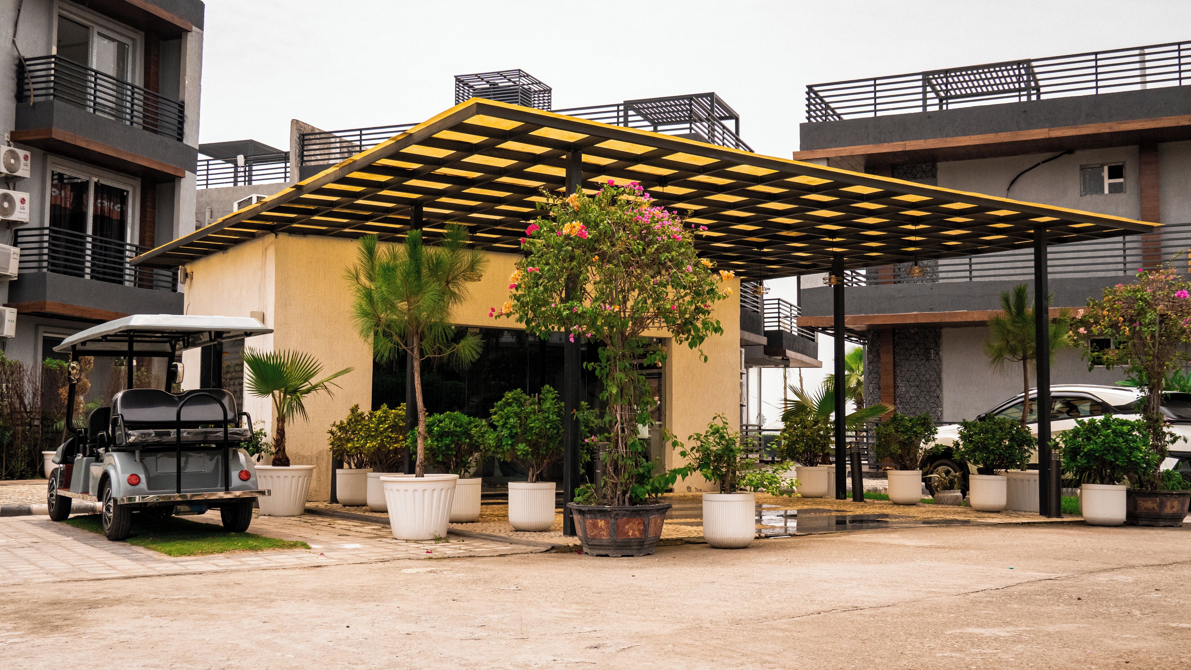 A modern building with a covered parking area, potted plants, and a golf cart.